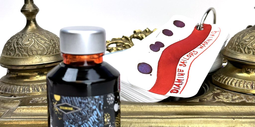 Diamine Sailor's Warning ink swatches and writing sample on Col-o-ring ink testing card resting on top of a vintage brass inkwell with the Diamine ink bottle in the front to the side. 