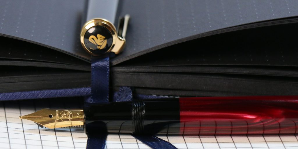 Pelikan Classic 200 Special Edition Red Marbled fountain pen uncapped with gold nib close-up on black dot grid paper.