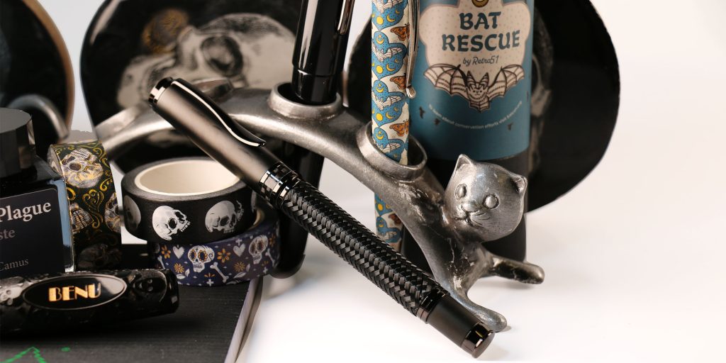 Monteverde Innova Formula M black fountain pen with silver cat pen holder, Wearingeul The Plague ink, and Retro51 Bat Rescue pen in background.