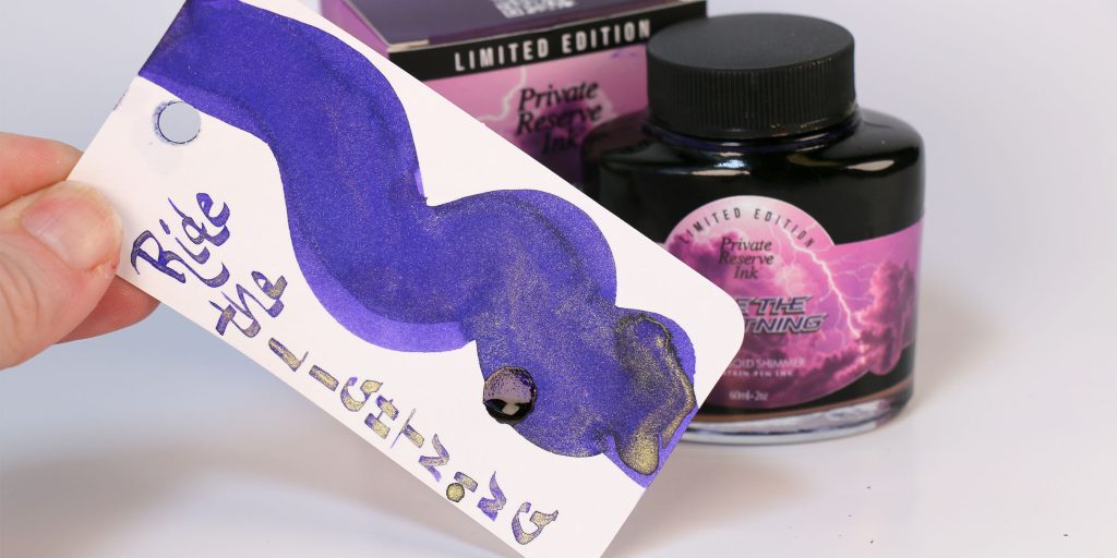 The gold shimmer shining through the dark purple ink of Private Reserve Ride the Lightning ink on the Col-o-ring swatch card with bottle and box behind. 