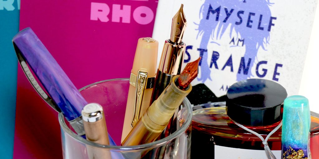 Hinze The Gentleman fountain pen, Penlux Elite Queen fountain pen, Visconti Persephone fountain pen, and Kaweco Sport fountain pen - all in a clear pen cup.