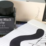 Wearingeul The Black Tulip glistening fountain pen ink bottle with a dark black ink swatch in a grid notebook.