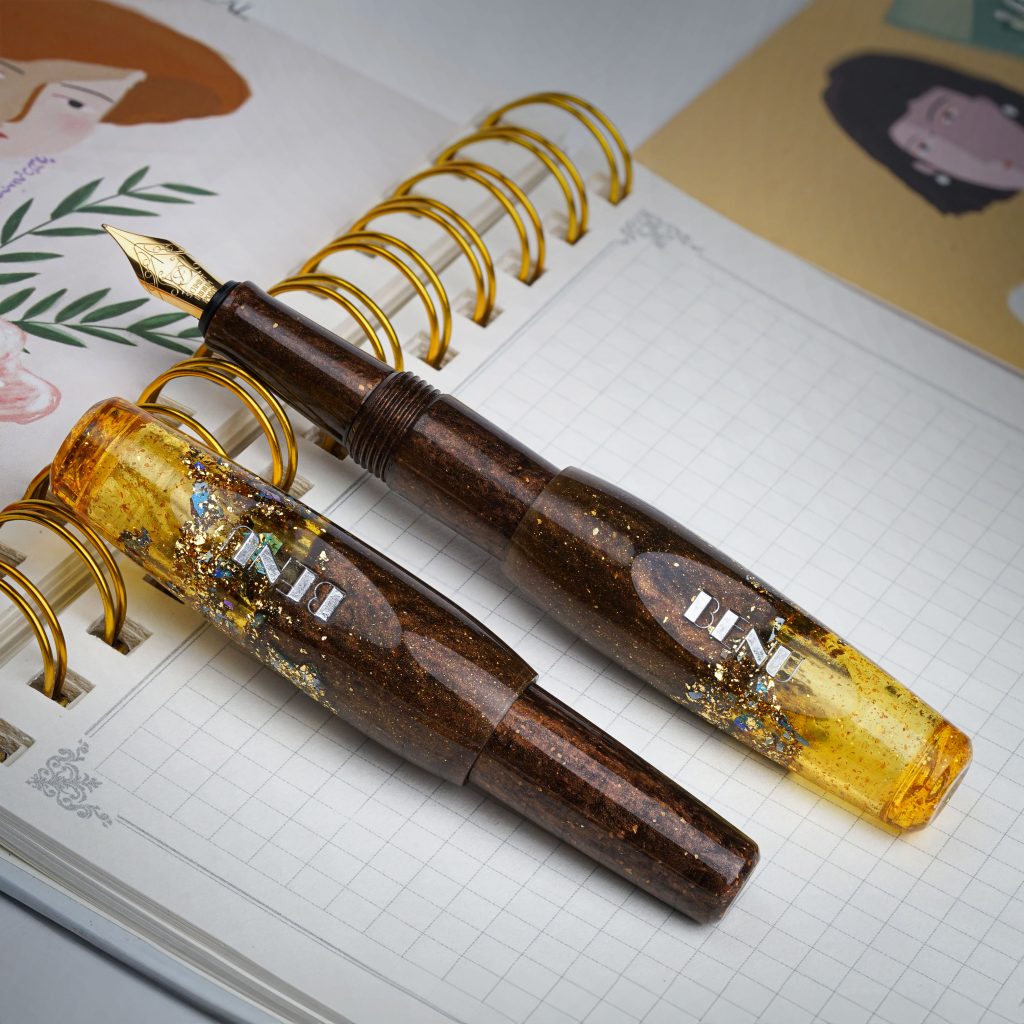 Benu Pixie Honey Bronze fountain pen uncapped and resting on the gold spiral portion of an open notebook.