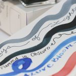 Ink swatches in a notebook featuring Tono & Lims Flammd in Obscuro with layered blue, black, gray, and coral fountain pen inks.