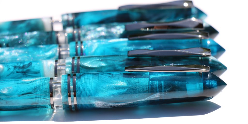 Gioia Metis World Oceans Southern fountain pens showing off the stunning Jonathan Brooks resin inspired by the Southern Ocean from the side with several capped fountain pens lined up.