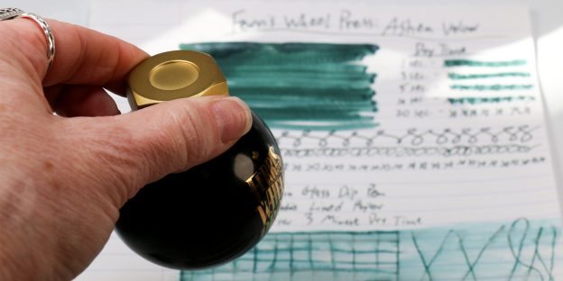 Ferris Wheel Press Ashen Valour 20ml fountain pen ink bottle held aloft above the full sheet of test results in the Pen Chalet Ferris Wheel Press Ashen Valour ink review.