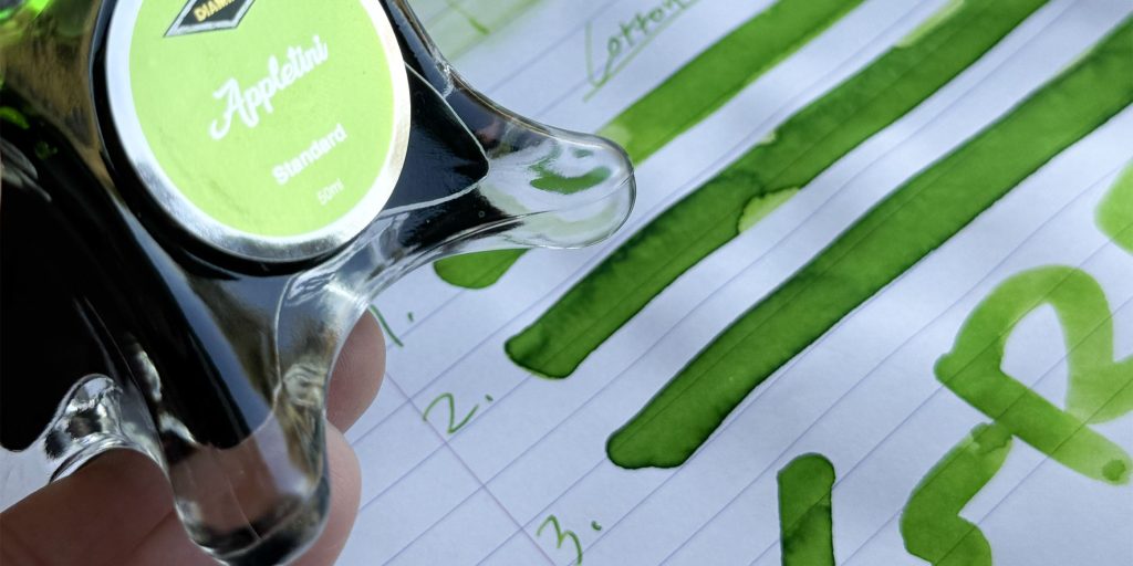 Diamine Appletini 50ml glass ink bottle displayed over vibrant apple-green swatches on Rhodia lined paper.