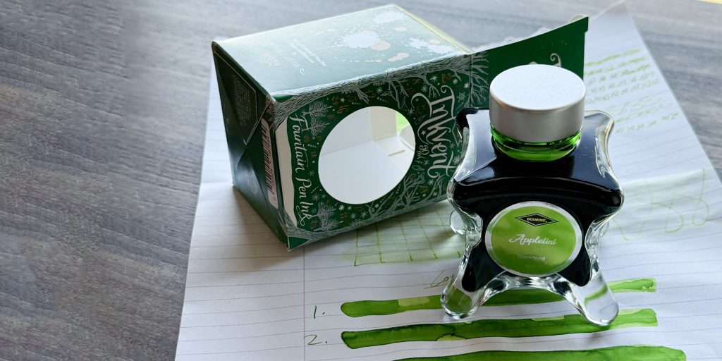 Diamine Appletini 50ml glass bottle alongside its decorative green Inkvent Edition packaging.